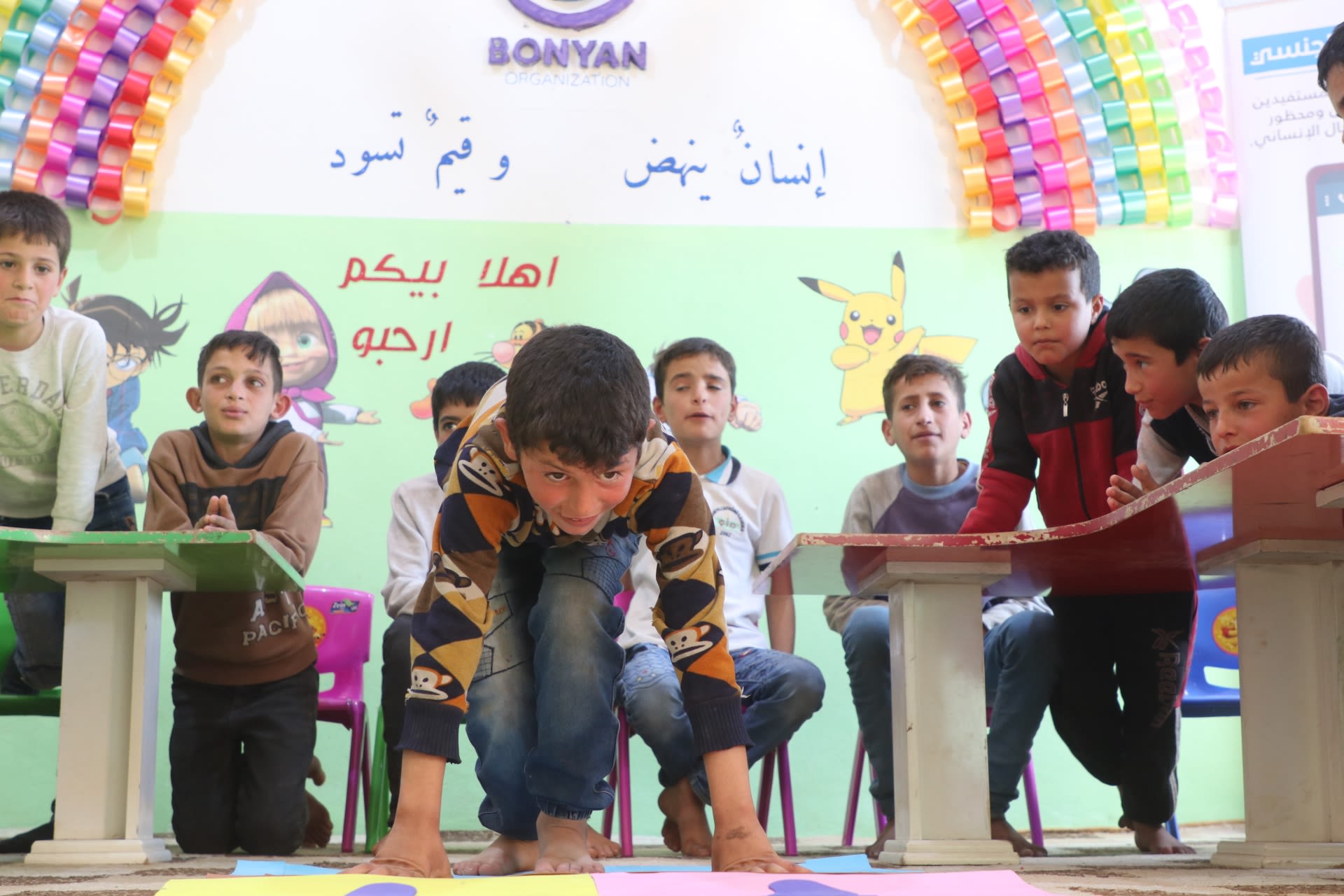 Kareem is bending down to take part in an activity surrounded by his classmates in a brightly-coloured safe learning space